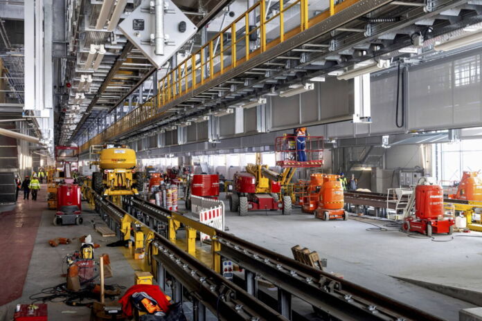 Das Werk eines Zulieferers für Fahrzeuge und Autoteile. Man sieht den Innenausbau der Halle des Konzerns. Darin stehen verschiedene Maschinen und Fahrzeuge.