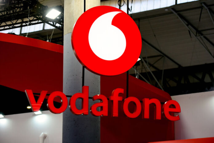 Das Vodafone-Logo mit dem untenstehenden Schriftzug am Eingang eines Shops. Hier können Kunden Handys mit und ohne Vertrag sowie verschiedene Tarife für Internet und Telefonie kaufen.