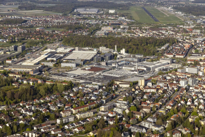 Eine Luftaufnahme von einem großen Industriegebiet. Darauf sind zahlreiche Hallen und Gebäude von großen Unternehmen zu sehen. Man sieht auch die umliegenden Wohngebiete.