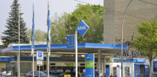 Eine Aral-Tankstelle steht neben einem Gebäude. Die Preise sind auf der Anzeigetafel ausgeschrieben. Zwei Autos stehen auf dem Gelände der Tankstelle.