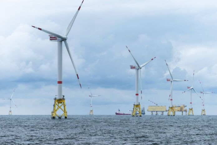 Ein großer Soffshore Windpark mit Windrädern auf dem Meer. Es stehen mehrere große Windräder nebeneinander und erzeigen Energie aus Windkraft.