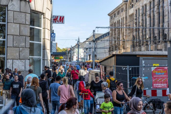 In der Karlsruher Innenstadt tummeln sich zahlreiche Menschen an einem verkaufsoffenen Sonntag. Im Hintergrund stehen gelbe Sonnenschirme, die offensichtlich zu einem Lokal gehören und die Vorbeigehenden zum Verweilen einladen.