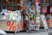 Eine ältere Kundin steht vor einer Buchhandlung in der Innenstadt und stöbert durch die Körbe mit Kalendern. Neben ihr befinden sich verschiedene reduzierte Kalender sowie weitere Bücher und sonstige Ware.