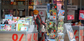 Eine ältere Kundin steht vor einer Buchhandlung in der Innenstadt und stöbert durch die Körbe mit Kalendern. Neben ihr befinden sich verschiedene reduzierte Kalender sowie weitere Bücher und sonstige Ware.