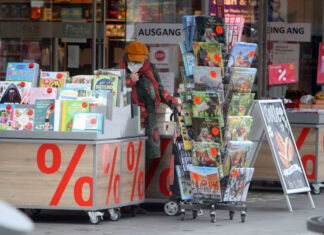 Eine ältere Kundin steht vor einer Buchhandlung in der Innenstadt und stöbert durch die Körbe mit Kalendern. Neben ihr befinden sich verschiedene reduzierte Kalender sowie weitere Bücher und sonstige Ware.
