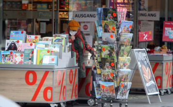 Eine ältere Kundin steht vor einer Buchhandlung in der Innenstadt und stöbert durch die Körbe mit Kalendern. Neben ihr befinden sich verschiedene reduzierte Kalender sowie weitere Bücher und sonstige Ware.