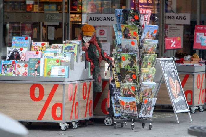 Eine ältere Kundin steht vor einer Buchhandlung in der Innenstadt und stöbert durch die Körbe mit Kalendern. Neben ihr befinden sich verschiedene reduzierte Kalender sowie weitere Bücher und sonstige Ware.