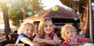 Drei Kinder essen etwas gemeinsam, sie haben Spaß miteinander. Es handelt sich wohl um eine kinderfreundliche Mahlzeit, denn allen scheint es zu schmecken.