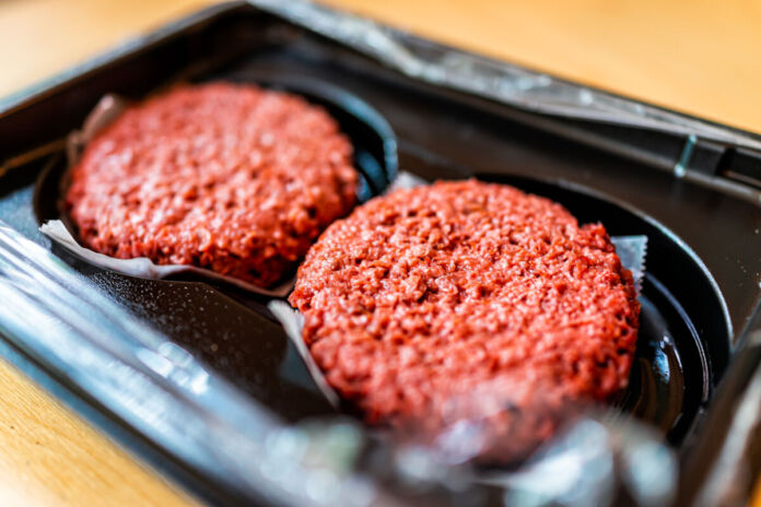 Eine Nahaufnahme von zwei Patties für Burger. Es handelt sich dabei um veganes Hackfleisch, welches noch ungebraten, in einer Verpackung aus Kunststoff liegt. Später entstehen daraus vegane Burger.