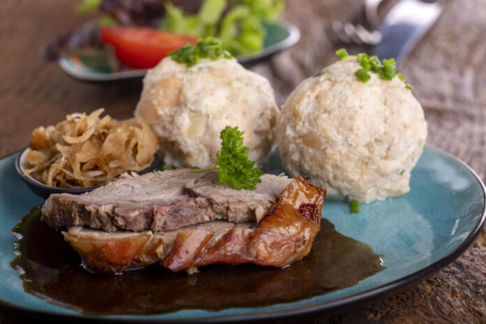 Auf dem Teller liegen Schweinebraten, Soße und Knödel zusammen. Das ist ein traditionelles Gericht aus der Wirtsstube. Auch in vielen Brauereien steht es auf der Speisekarte. Im Mittelpunkt steht das Fleisch.