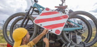 Ein Mann befestigt ein Fahrrad auf einem Fahrradträger, um Fährräder mit dem Auto zu transportieren. Er bringt auch ein Warnzeichen an.