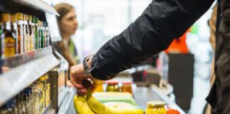 Eine Person geht im Supermarkt einkaufen. Sie legt Bananen und weitere Artikel auf das Band an der Kasse. Der Kunde bezahlt und verlässt den Supermarkt.