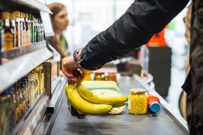 Eine Person geht im Supermarkt einkaufen. Sie legt Bananen und weitere Artikel auf das Band an der Kasse. Der Kunde bezahlt und verlässt den Supermarkt.