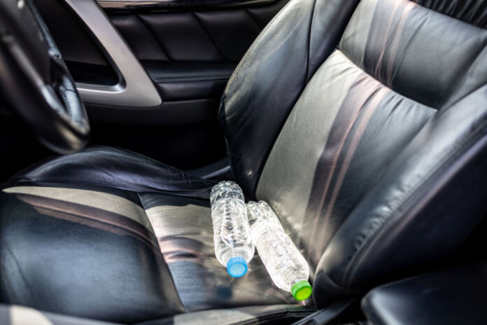 Zwei volle Wasserflaschen liegen auf schwarzem Leder auf dem Beifahrersitz in einem Auto. Auf die Flaschen scheint die pralle Sonne.