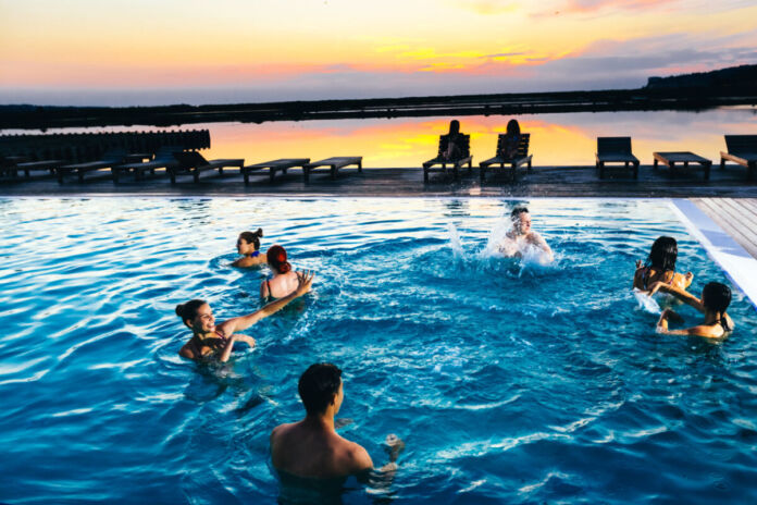 Verschiedene Menschen schwimmen mitten in der Nacht in einem Schwimmbad oder in einem Swimmingpool gemeinsam. Sie planschen und haben Spaß im Wasser.