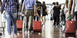 Viele Männer und Frauen befinden sich in der Abflughalle eines Flughafens und ziehen ihr Gepäck Richtung Gate. Die Reisenden sind auf dem Weg in den Urlaub.