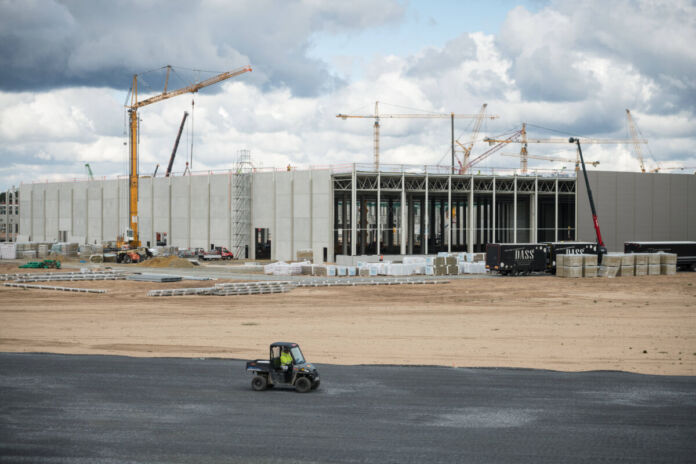 Auf diesem Bild entsteht eine große Gigafactory. Noch befindet sie sich mitten in der Bauphase. Deshalb sieht man Baufahrzeuge und ein unfertiges Fabrikgebäude. Aber schon bald werden hier Elektroautos produziert.