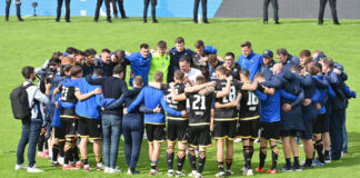 Mehrere Spieler einer Fußballmannschaft stehen gemeinsam Arm in Arm in ihren Trikots auf dem Fußballplatz. Die Bundesliga-Spieler bereiten sich auf das Fußballspiel vor.