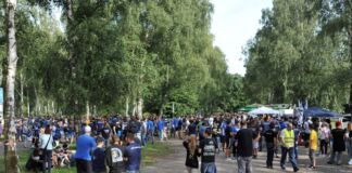 Viele Karlsruher SC Fans strömen zum Fußballspiel ihres Vereins. Sie tragen Fan-Shirts und Trikots. Die Kleidung und die Fanartikel sind in den Vereinsfarben blau und weiß gehalten.