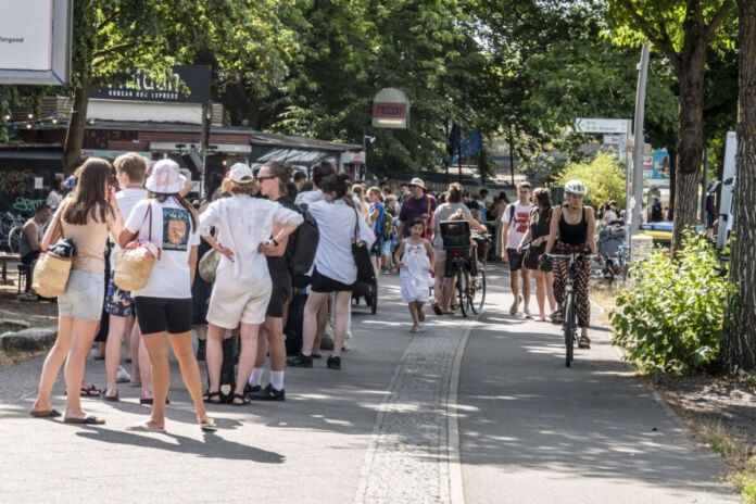 Es gibt einen großen Andrang und auch eine lange Schlange von Menschen, die hintereinander anstehen, um eine Fahrkarte oder gar Einlass zu erhalten. Sie warten lange gemeinsam. In der Schlange stehen Erwachsene, Jugendliche und Kinder.