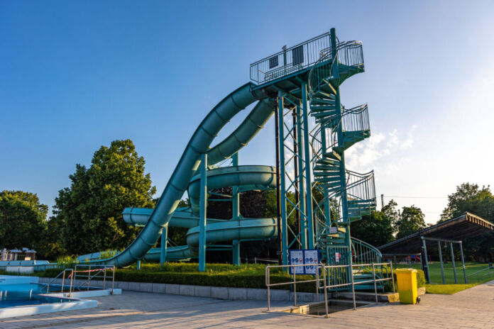 Eine lange Wasserrutsche steht mitten in einem Freibad. Für Besucher ist die Rutsche in dem Schwimmbad eine tolle Attraktion für heiße Tage.