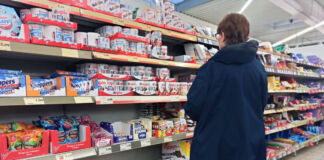 Eine Frau steht in einem Discounter oder Supermarkt vor einem Regal voller Süßigkeiten. Es sind Schokolade und andere Artikel bekannter Marken zu sehen.