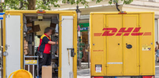 Ein Paketzusteller steht in seinem Fahrzeug von DHL und sortiert Briefe und Pakete. Viele größere und kleinere Pakete sind in Regalen an den Wänden des Fahrzeugs aufgereiht und aufeinander gestapelt. Wegen des Gewichts so manches Pakets bekommen immer mehr DHL-Paketboten Rückenprobleme.