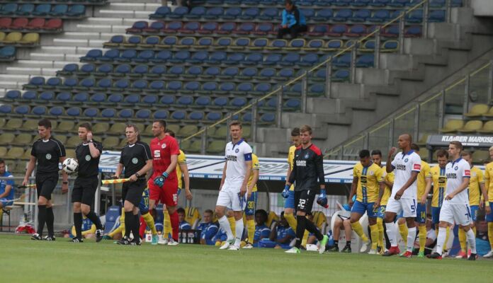 Die Spieler des Karlsruher SC laufen in ein leeres Stadion zu einem Spiel oder einem Testspiel in der Bundesliga auf. Daneben stehen die Trainer des KSC ebenso wie die Schiedsrichter des Tages.