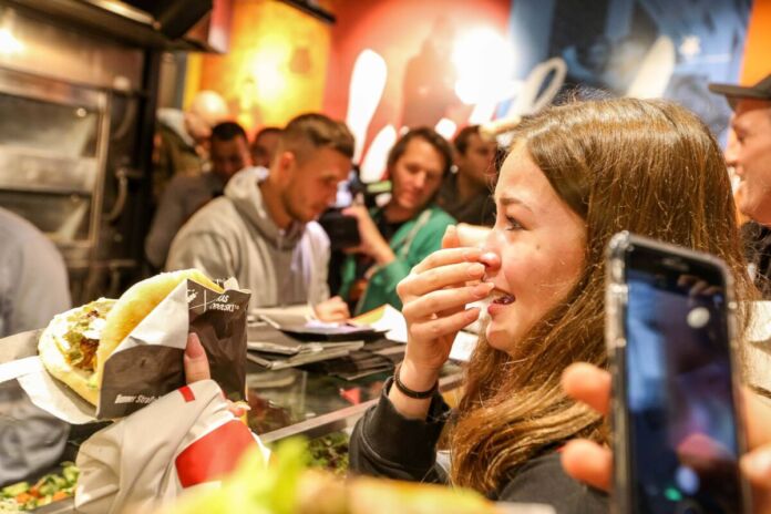 Junges Mädchen nimmt mit Freudentränen in den Augen einen Döner Kebab bei der Eröffnung eines Dönerladens entgegen. Im Hintergrund steht Lukas Podolski.