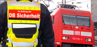 Ein Sicherheitsbeamter steht an einem Bahnhof vor einem roten Zug und überwacht den Bahnhof. Der Mann ist von hinten zu sehen und trägt eine gelbe Warnweste und sorgt für Sicherheit an einem zu gefährlichen Bahnhof.