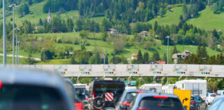 Zahlreiche Fahrzeuge passieren eine Mautstelle auf einer Autobahn. Das Verkehrsaufkommen ist hoch, der Verkehr fließt zähflüssig und es droht ein Stau.