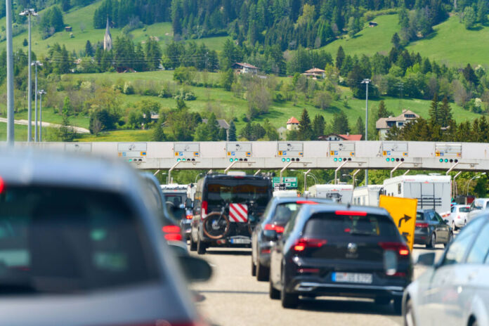 Zahlreiche Fahrzeuge passieren eine Mautstelle auf einer Autobahn. Das Verkehrsaufkommen ist hoch, der Verkehr fließt zähflüssig und es droht ein Stau.