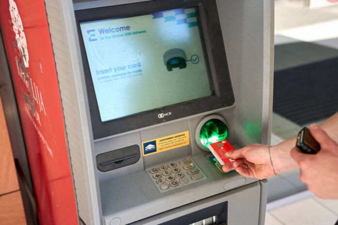 Eine Hand steckt eine Giro-Karte in einen Geldautomaten der Sparkasse, weil Geld abgehoben wird. Auf dem Bildschirm steht in englischer Sprache, dass man seine Karte einstecken soll.