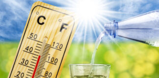 Eine Person schüttet Wasser in ein Wasserglas ein, im Hintergrund ist ein Thermometer zu sehen, dass hohe Temperaturen anzeigt. Außerdem scheint die Sonne in gleißendem Licht.