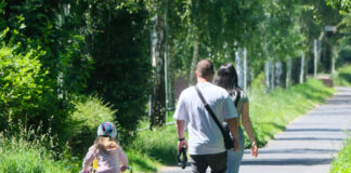 Mutter und Vater gehen gemeinsam mit ihrem Kind spazieren. Das Kind fährt auf einem kleinen Kinderfahrrad mit Stützräder nebenher. Sie verbringen gemeinsame Familienzeit.