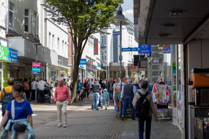 An einem offensichtlichen Tag des Wochenendes bummeln viele Menschen durch die Innenstadt und laufen an den offenen Geschäften vorbei. Einige kommen mit Einkaufstüten aus den Läden. Die Fußgängerzone ist gut besucht.