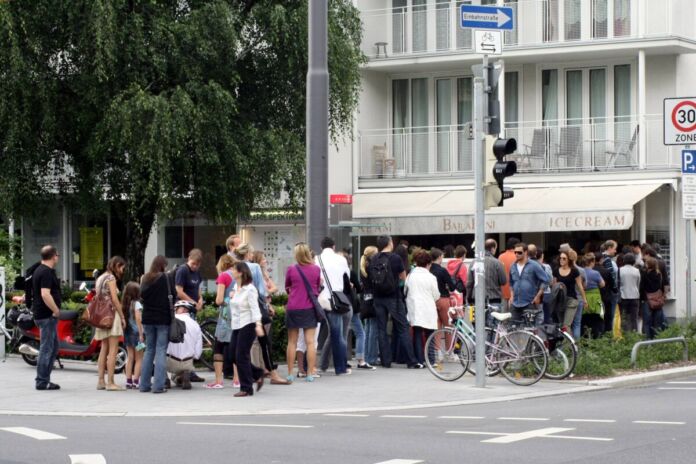 Viele Menschen stehen Schlange und warten auf Einlass oder den Verkauf von Produkten. Dies ist eine Eisdiele, in der es wahrscheinlich sehr gutes Eis gibt. Deshalb stehen so viele Leute an.