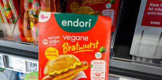 Die Hand von einem Kunden hält vor einem Supermarkt-Regal eine Packung eines Fleischersatzproduktes in einer Hand. Es sind vier vegane Bratwürste von endori verpackt. Eine Supermarktkette will nun weitere Filialen auf vegan umstellen.