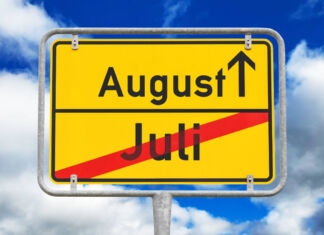 Im Vordergrund befindet sich ein gelbes rechteckiges Schild, das mit einem waagerechten schwarzen Strich in zwei Felder unterteilt ist. Auf dem unteren steht Juli geschrieben und ist mit einem roten Balken diagonal durchgestrichen. Auf dem oberen Feld steht August und ein Pfeil zeigt nach oben. Im Hintergrund ist ein blauer Himmel mit Wolken zu sehen.