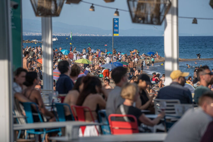 Mehrere Urlauber feiern gemeinsam am Strand. Viele Touristen sind am Meer, um zu baden und Urlaub zu machen. Die Strandpromenade ist ebenfalls überfüllt.