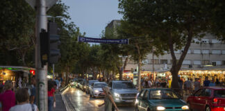 Mehrere Fußgänger gehen über eine mehrspurige Straße über die Ampel. Es dämmert schon und die Autos haben ihre Scheinwerfer an. Im Hintergrund sieht man einen beleuchteten Markt. Eine neue Bußgeldwelle kommt nun auf Millionen Autofahrer zu.