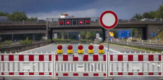 Auf einer leeren Autobahn ist eine rot-weiße Baustellenabsperrung zu sehen, die die Straße für den Verkehr sperrt. Ein Haltestoppschild weist extra darauf hin, dass hier nicht gefahren wird.