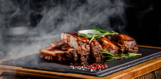 Ein Schiefertafel mit Grillfleisch in einem Grillrestaurant dampft appetitlich. Dazu gibt es Rosmarin als Gewürz, das Fleisch wurde auf dem Stein erhitzt.