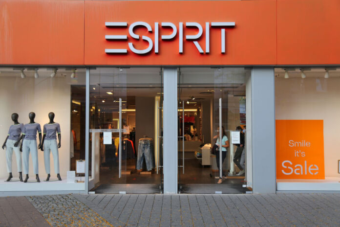 Die Frontansicht von einem Esprit-Mode-Laden in den Farben orange und grau. Im Schaufenster stehen die Modepuppen. Im Innenraum des Ladens wird Kleidung verkauft.