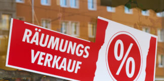 Im Schaufenster eines Geschäftes ist ein Schild angebracht, auf dem "Räumungsverkauf" in Weiß auf rotem Hintergrund steht. Daneben ist ein Prozentzeichen abgebildet. Offensichtlich schließt das Geschäft bald.