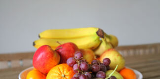 Eine Schale mit frischem Obst und Früchten steht auf einem Tisch. Darunter befinden sich Bananen, Äpfel, Orangen und Weintrauben.