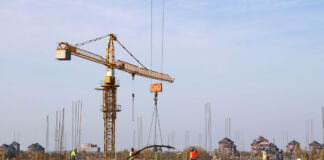 Eine große Baustelle, auf der ein Kran im Einsatz ist. Unten arbeiten die Bauarbeiter und stellen die Gerüste auf. Ein neues großes Gebäude oder ein Hochhaus aus Betonelementen entsteht.