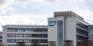 Auf dem Bild ist ein modernes Bürogebäude zu sehen, das die Firmenzentrale der SAP darstellt. Das Gebäude hat eine helle Fassade und viele Fenster. Auf der rechten Seite des Gebäudes ist das große, blau-weiße SAP-Logo gut sichtbar.