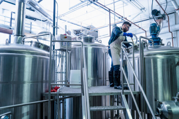 Ein Mitarbeiter kontrolliert die Getränkeproduktion in den großen Kesseln der Fabrik. Er klettert auf die Leiter und sieht sich den Inhalt der Fässer an.