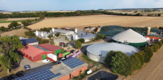 Aus der Luft aufgenommes Bild einer großen Biogsasanlage mit riesigen Silos und vielen Bauernhäusern. Weiterhin gibt es dort viele Ställe und große Felder in der Umgebung.